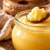 A glass jar of grainy golden desi ghee with a wooden spoon
